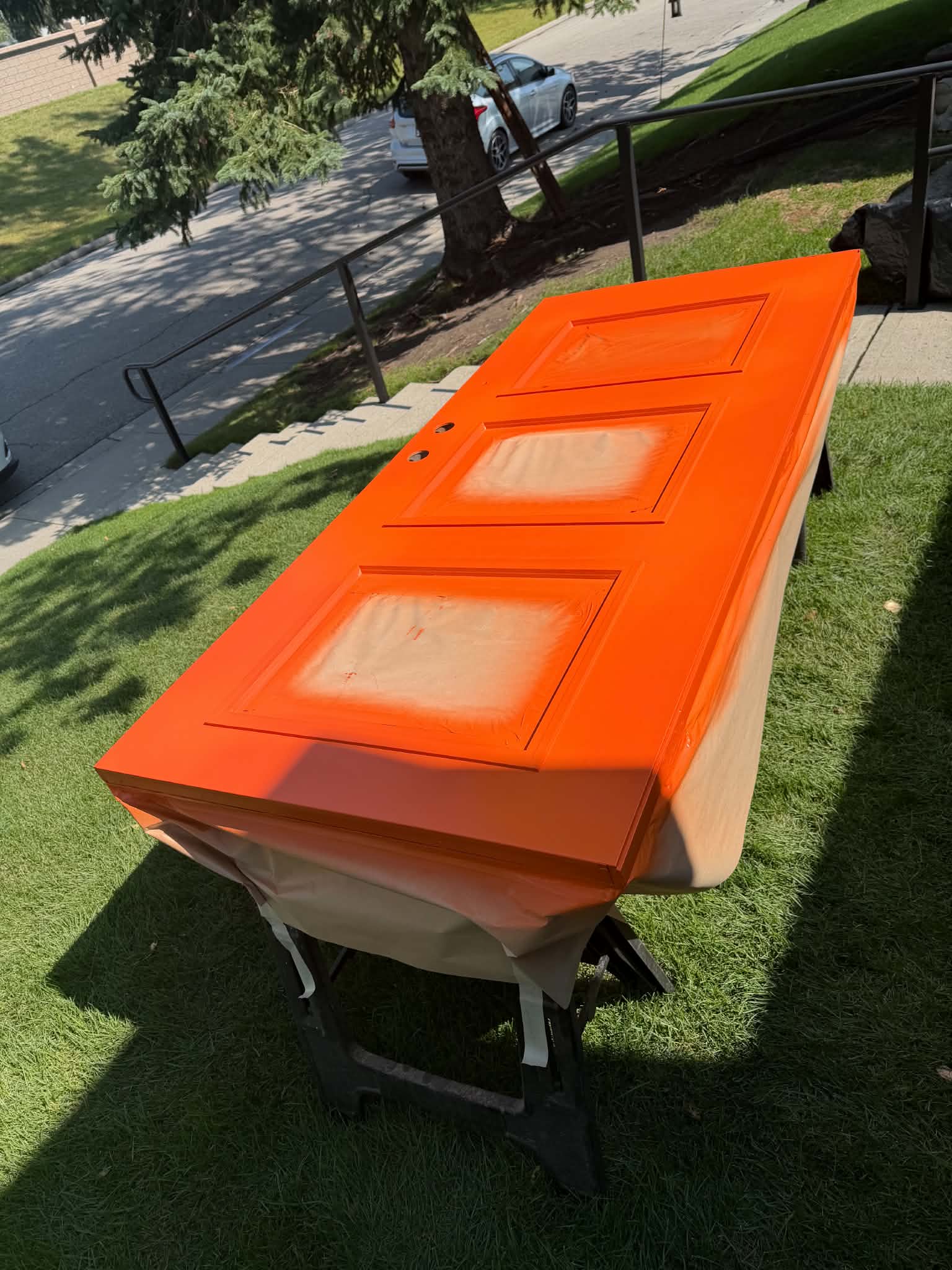 Door freshly painted orange, laid flat on sawhorses outdoors