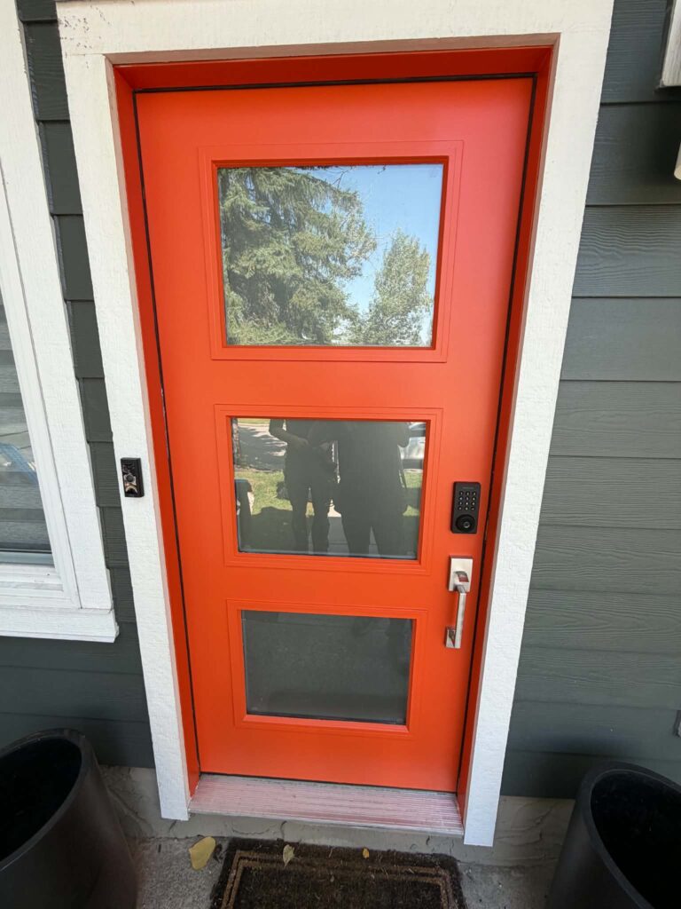 Front entry door painted bright orange against grey siding