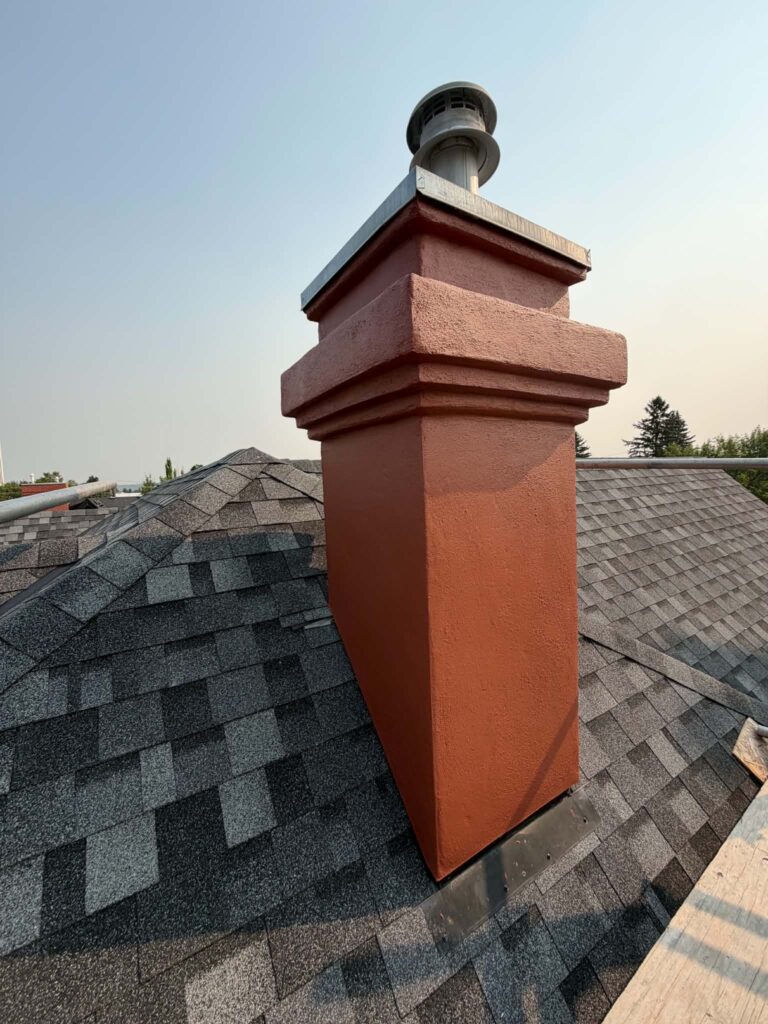 Finished red chimney from a second angle, showing the textured finish, banded top section and metal flashing at the roof