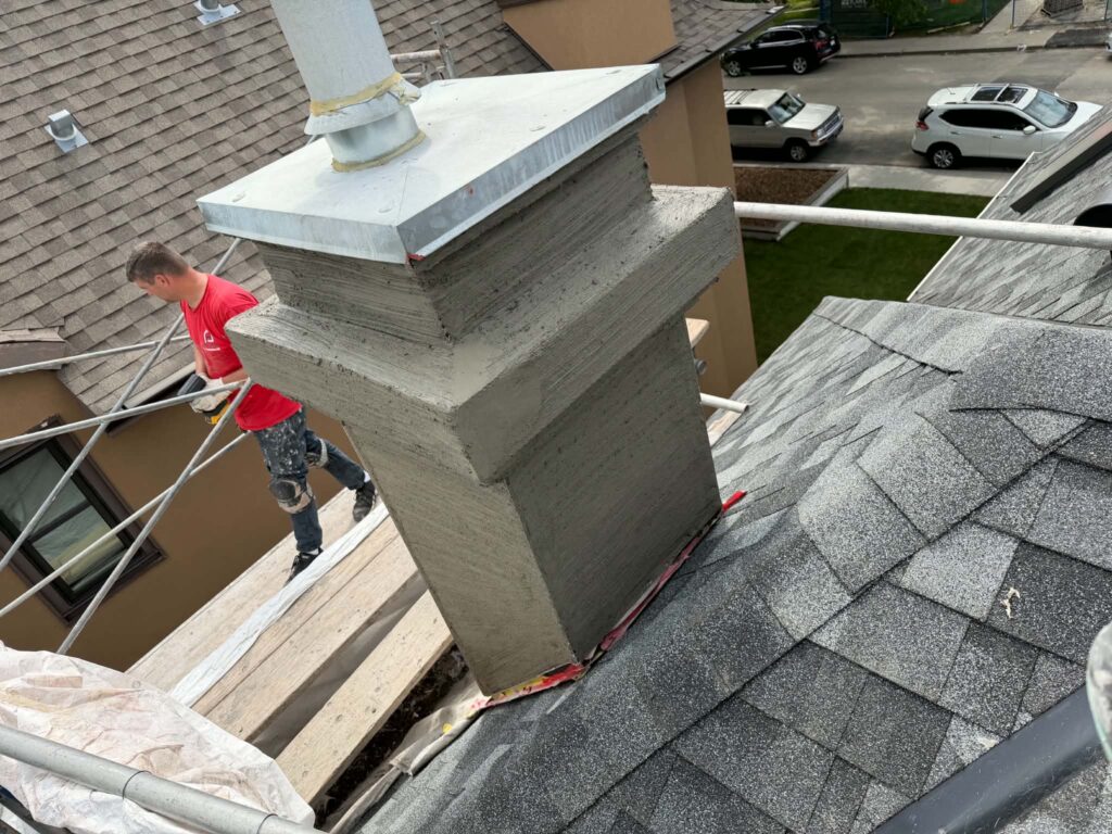 Chimney covered in a fresh grey base coat with horizontal scratch lines, with a worker on the scaffolding beside it