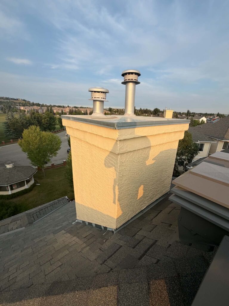 Cream stucco chimney with two vent caps after exterior repair